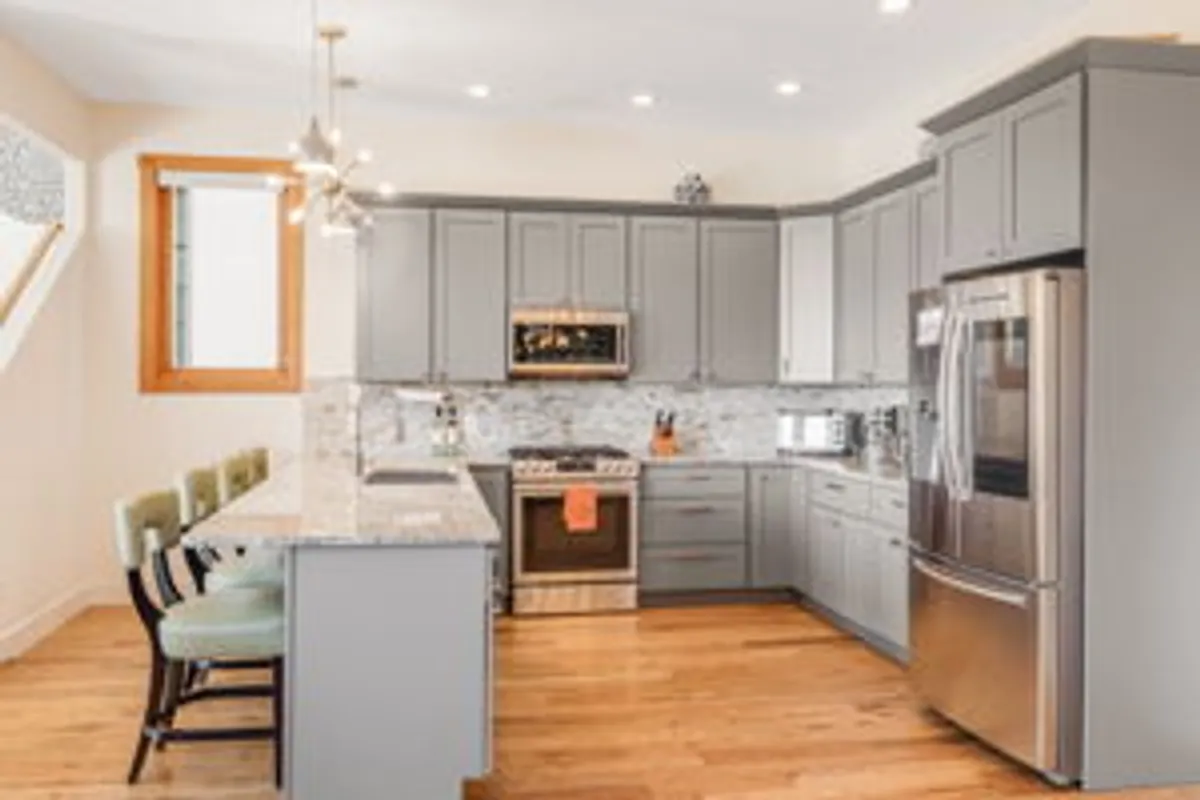 This image features a modern kitchen centered around a spacious island, with stainless steel appliances, sleek grey cabinetry, and granite countertops. The layout signals both functionality and style, perfect for preparing meals and gathering with family or friends. The inviting atmosphere suggests it is ideal for hosting culinary experiences.