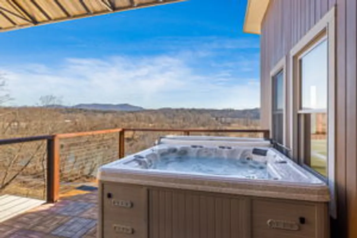 This exterior image features a hot tub on a rooftop deck overlooking sweeping mountain vistas. The deck railing frames the view, and the tranquil ambiance is enhanced by the expansive sky and distant landscape, evoking a sense of elevated retreat.