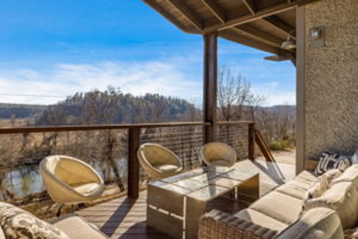 A serene exterior view featuring a comfortable outdoor seating area on a deck, with the river and mountains forming a breathtaking natural backdrop. The scene suggests opportunities for social gatherings or quiet moments immersed in nature.