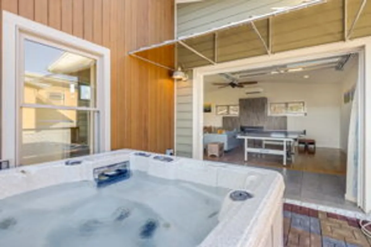 A hot tub occupies a stylish patio space adjoining an open room with wooden accents. The area is designed for relaxation and entertaining, with ample seating for guests to enjoy the sunset or a quiet soak while immersed in nature’s beauty.