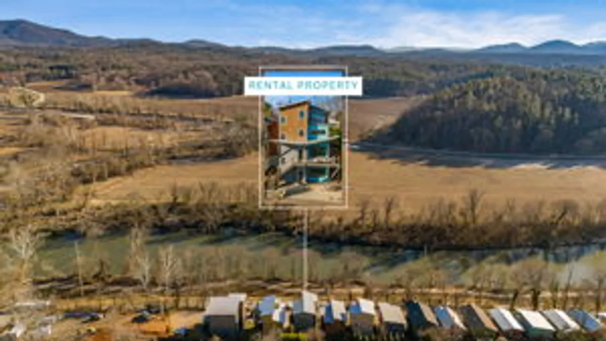 This image captures the rental property building set against the serene backdrop of the river and surrounding landscape. The balcony overlooks the water, with visible nature trails and woodlands nearby, suggesting immediate access to the outdoors and family adventures. The setting sun casts a warm glow, emphasizing the peaceful, scenic atmosphere.