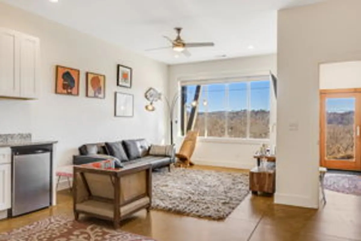 A welcoming living space with a large window offering an expansive view, a comfortable sofa, wooden coffee table, and wall art. The room radiates warmth and is designed for relaxing while soaking in the surrounding landscape, ideal for enjoying a sunset cocktail or quiet conversation.