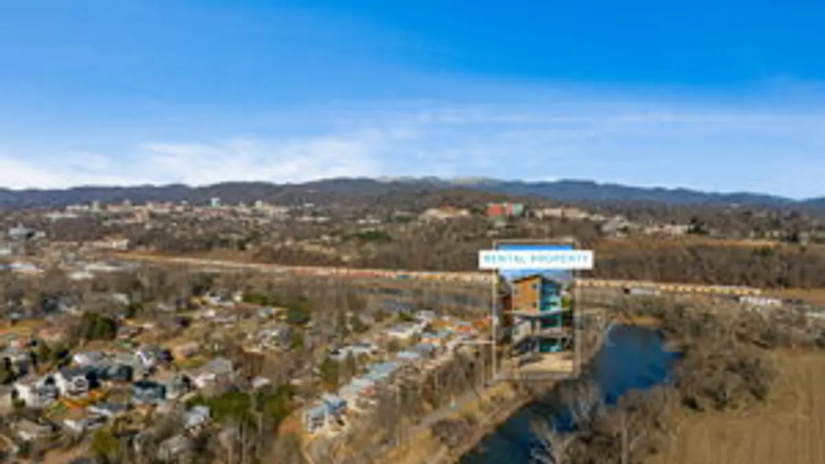 The image showcases the rental property with the river in the foreground and the city skyline in the distance. The lush landscape and riverside setting evoke a sense of both tranquil escape and easy access to Asheville's urban and cultural attractions, like the Biltmore Estate.